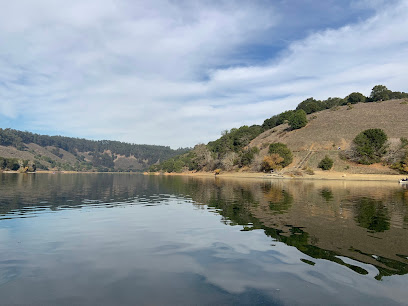 Calm lake water reflecting sky and hillside with scattered trees at Chabot Park