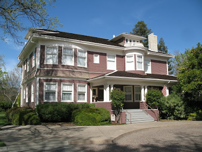 Historic two-story brick house with front porch and landscaped grounds under clear sky
