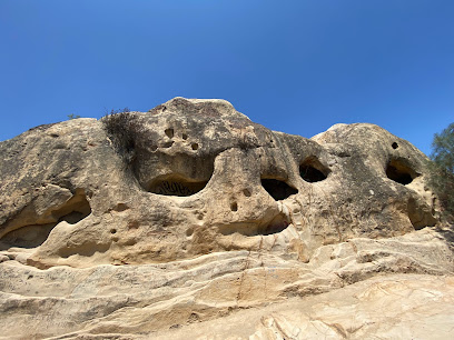 Natural rock formation with multiple cave openings in desert landscape under clear blue sky