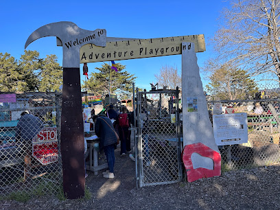 Entrance gate to Adventure Playground with decorative metal arch and chain-link fence on clear day