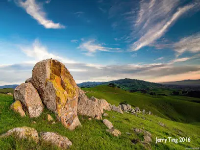 Rolling green hills with large boulders and blue sky with wispy clouds
