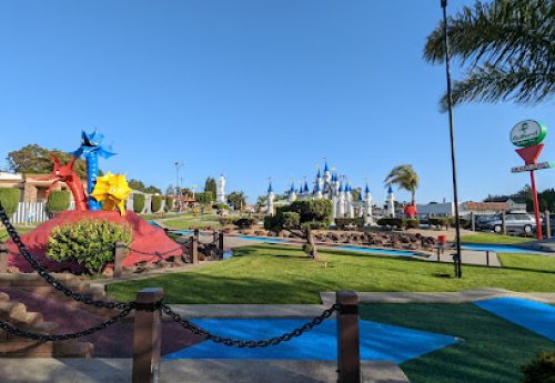 Mini golf course with colorful obstacles and castle in background under clear blue sky
